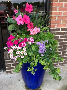 a blue vase filled with lots of different colored flowers next to a brick wall and door