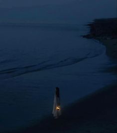 a woman standing on the beach at night holding a lantern in her hand and looking out to sea