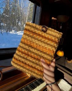 a person holding up a piece of knitted material in front of a piano keyboard