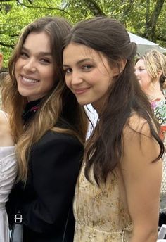 two young women standing next to each other in front of an outdoor area with people