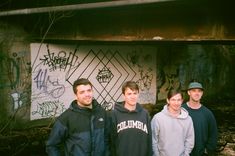 four men standing in front of graffiti covered wall