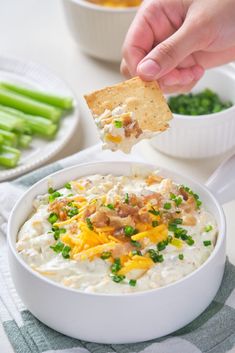 a person holding a cracker over a bowl of dip with asparagus and cheese