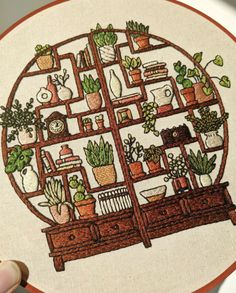 someone is holding up a cross - stitch pattern with plants in the shape of a bookcase