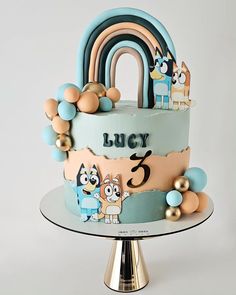 a birthday cake decorated with cartoon characters and rainbows on a silver plate, against a white background