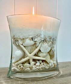 a candle that is sitting inside of a glass vase filled with shells and starfish