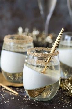 two glasses filled with liquid sitting on top of a table next to spoons and confetti