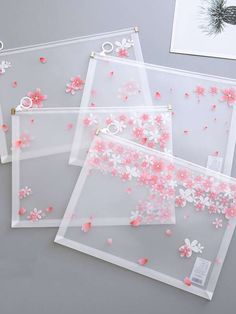 three clear acrylic bags with pink flowers on the inside and white petals on the outside