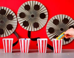 someone is holding a candy bar in front of three popcorn cups with fans on the wall behind them