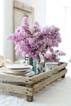 a tray with plates and vases filled with purple flowers sitting on top of a bed