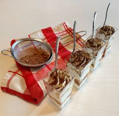 there are four desserts on the table with spoons next to it and a red checkered towel