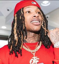 a man with dreadlocks wearing a red shirt and gold chain on his neck