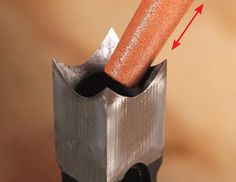 an orange piece of wood sticking out of a hole in a metal tool holder with two arrows pointing towards it