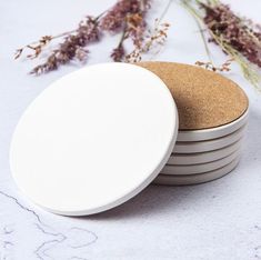 four white coasters stacked on top of each other with dried flowers in the background