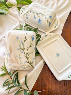 three white dishes with blue flowers and green leaves on them sitting on a wooden table