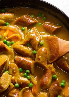 a pan filled with meat and vegetables covered in gravy next to a wooden spoon