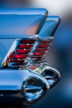 the rear end of an old car with chrome and red lights on it's hood