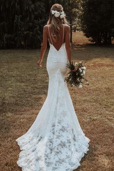 a woman in a white wedding dress is walking through the grass with her back to the camera