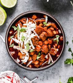 a bowl filled with meat and vegetables on top of a table next to sliced limes