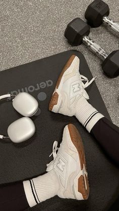 a pair of white shoes sitting on top of a black mat next to dumbbells