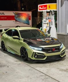 a green and black car parked in front of a gas station with no one around it