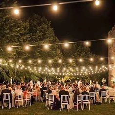 a group of people sitting at tables under string lights in front of an old building