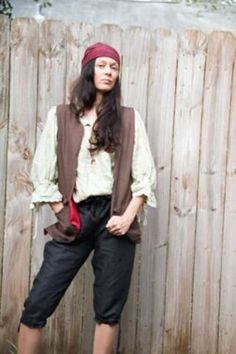 a woman standing in front of a wooden fence wearing pirate garb and holding a red purse