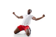 a man sitting on the ground with his arms in the air while wearing red shorts and a white t - shirt