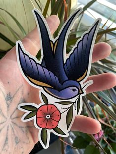 a hand holding a sticker with a blue bird on it's head and flowers in the background