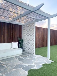 a white couch sitting under a pergolated roof next to a wooden fence and grass