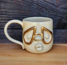 a white coffee cup with gold handles and two faces on the inside, sitting on a wooden surface