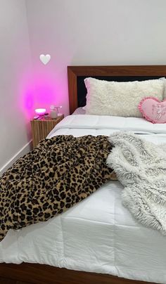 a bed with a leopard print blanket on top of it next to a pink light