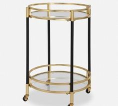 a round glass and metal side table with two shelves on each side, one shelf is black and the other is gold