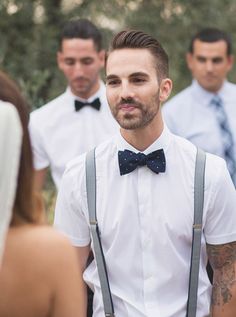 a man with suspenders and a bow tie standing in front of other men wearing white shirts