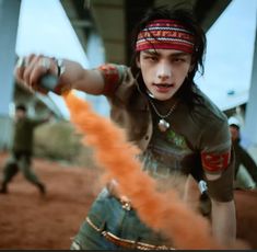 a young man holding a baseball bat in his right hand and wearing a bandana on top of his head