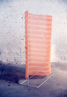 an orange piece of cloth sitting on top of a metal stand in front of a brick wall