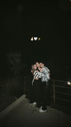 two people standing on a bridge at night with one person holding the other in his arms