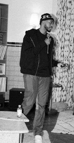 a black and white photo of a man standing in a living room holding a microphone