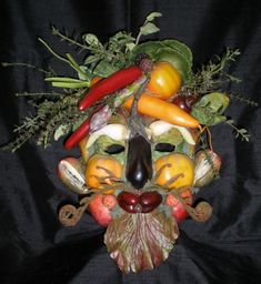 a mask made out of fruits and vegetables on a black cloth covered background with the image of a man's face