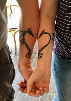 two people are holding hands with tattoos on their arms and one has a dragon tattoo on his arm