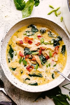 a bowl of soup with spinach, chicken and tomatoes on the side next to spoons