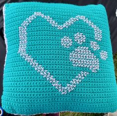 a blue crocheted pillow with a white heart drawn on the front and side