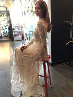 a woman sitting on top of a red chair in a white dress with long sleeves