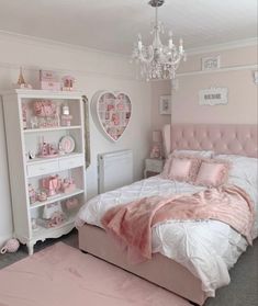 a bedroom decorated in pink and white with a bed, nightstands, shelves and chandelier