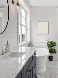 a white bathroom with marble counter tops and blue cabinetry, along with an oval bathtub