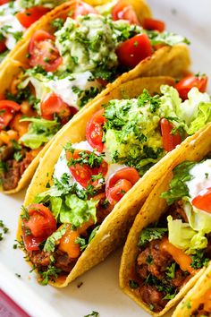 three tacos on a plate with lettuce, tomatoes and other toppings