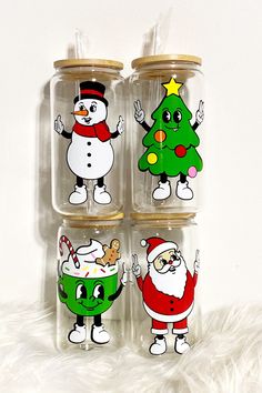 four christmas themed glass jars with santa claus, snowman and tree designs on them