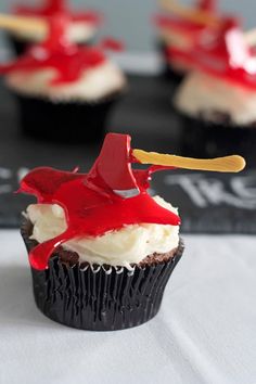 cupcakes with white frosting and red icing on top, sitting on a table