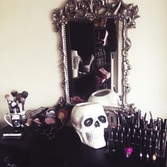 a skull is sitting in front of a mirror with makeup brushes and other items on it