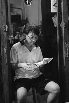 a man sitting on a chair reading a paper in front of his face and looking down