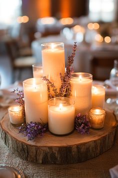 many lit candles are arranged on a wood slice with purple flowers and greenery in the center